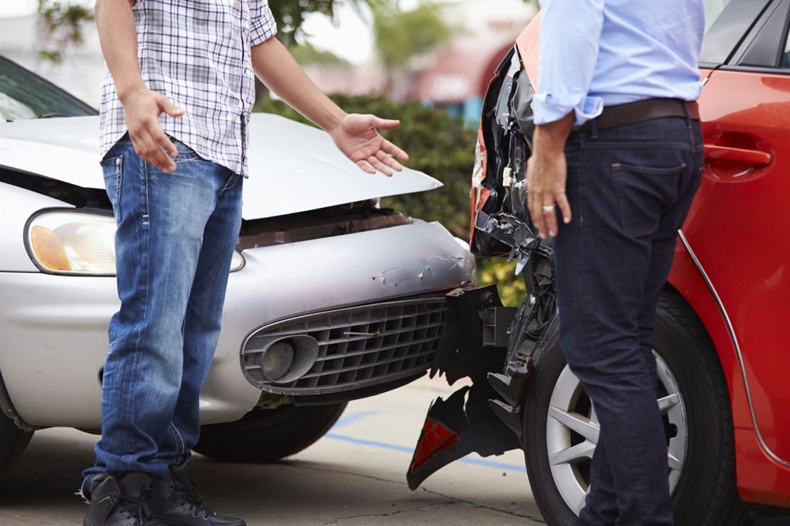 A couple of men standing next to a damaged car
Description automatically generated